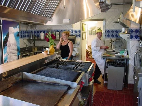Levitch designed Grégoire Piedmont kitchen with stainless hood, large griddle and range, blue and white tile walls, and staff working behind a warm wood service counter.