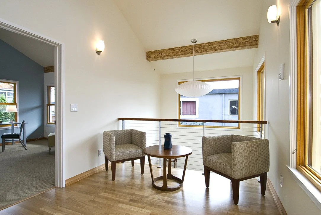 Second floor sitting area with wood floors, modern railing, and natural light, creating a quiet retreat that overlooks lower living spaces and reinforces the home’s open layout.