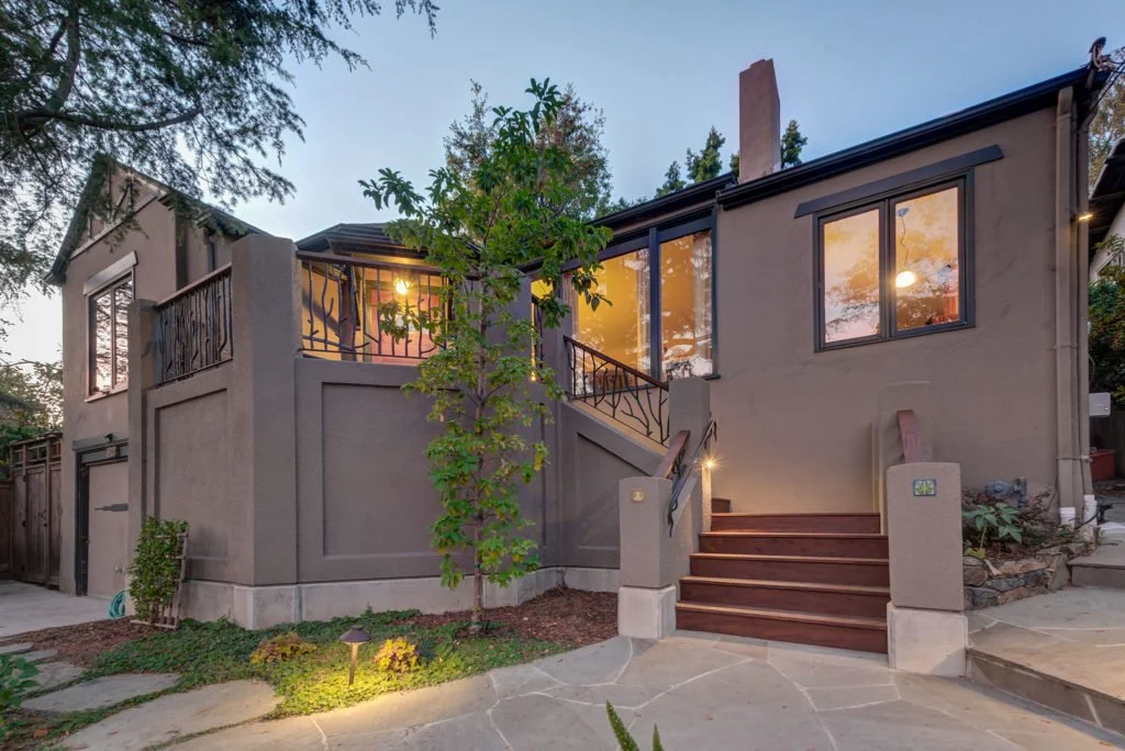 Front approach to the North Berkeley home showing broad lower steps rising to a deck and entry, with organic metal railing and landscaping integrated into the new design.