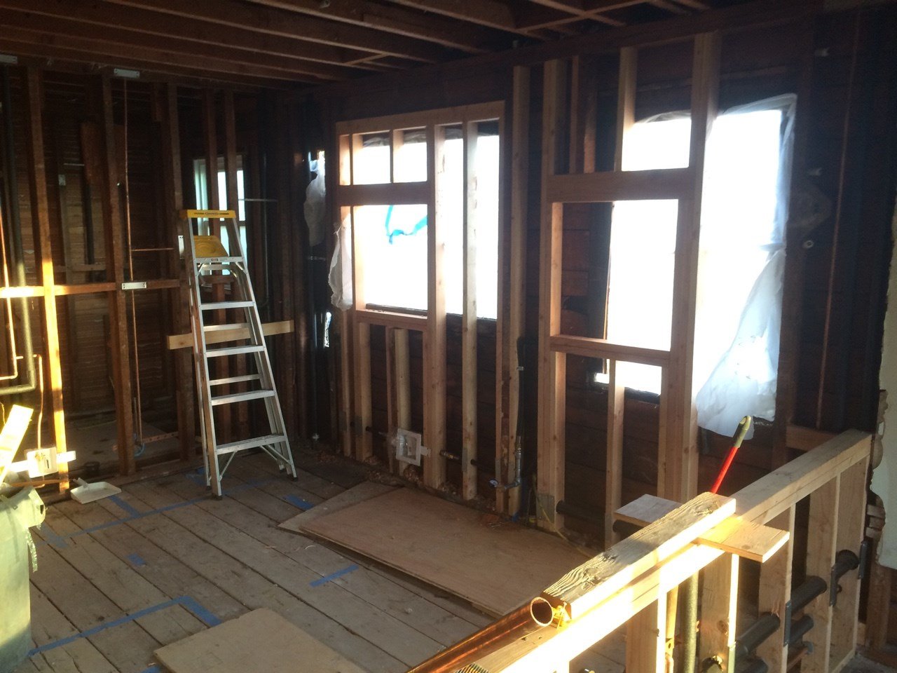 Interior stripped to studs during the Berkeley open plan remodel, with new window openings framed and a ladder on site, preparing for insulation, wiring, and finishes.