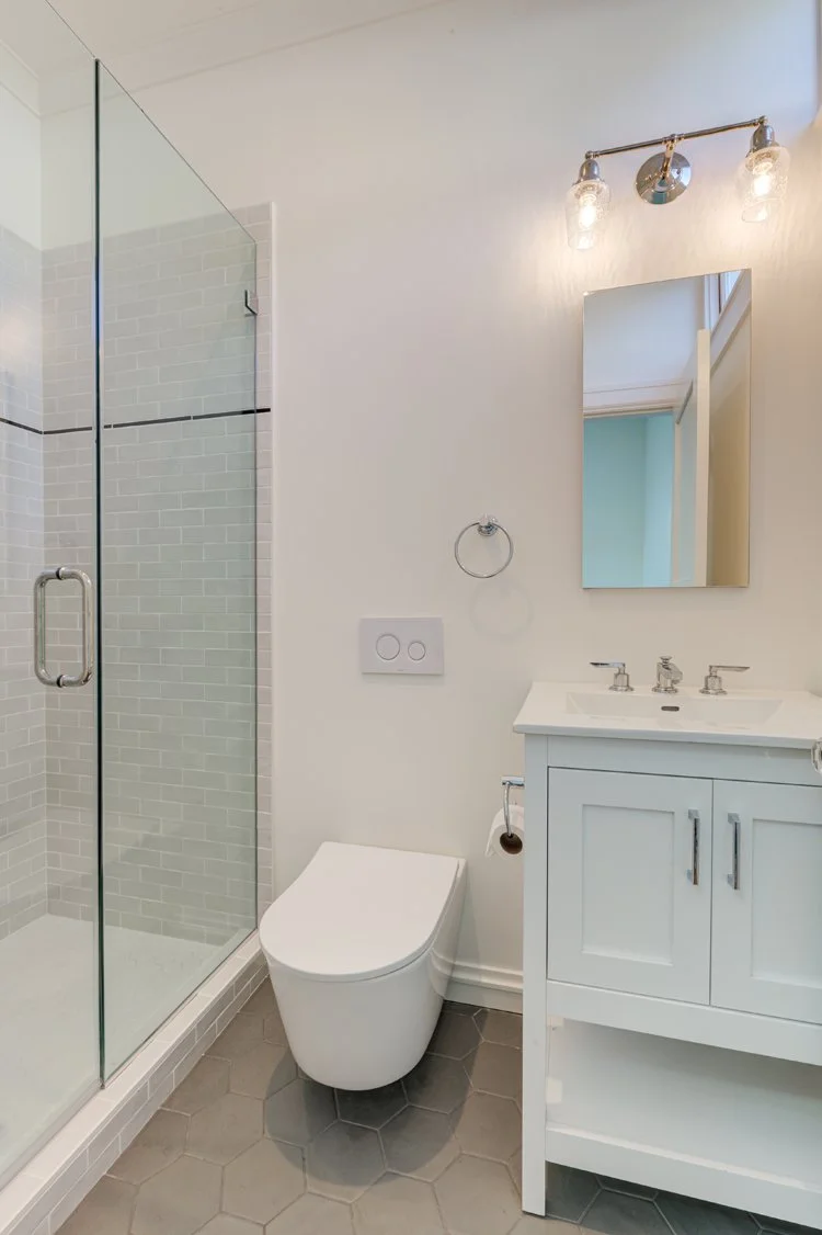 New full bathroom with glass-enclosed shower, hex tile floor, and compact vanity, created by relocating laundry and adding space while maintaining light and simplicity within the historic home.