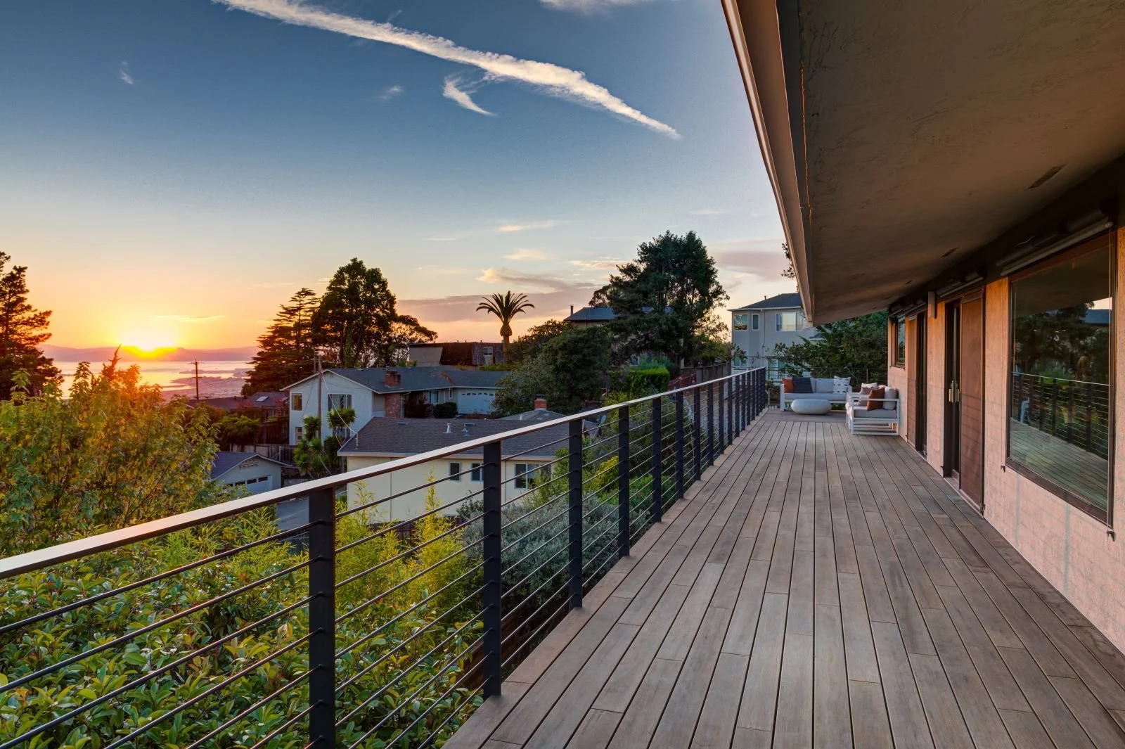 A long, linear deck emphasizes the home’s horizontal geometry, guiding views toward Bay views while reinforcing the rhythm of structure, railing, and cladding.
