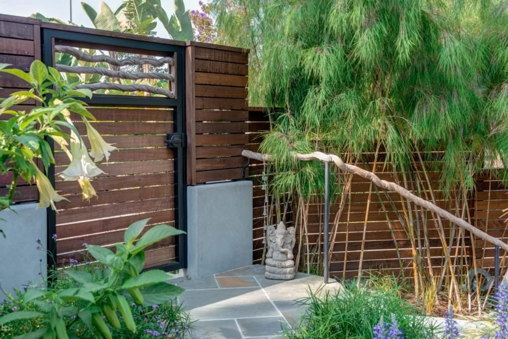 New wood fence and gate with a sculptural branch detail panel, set beside bamboo and garden planting, adding privacy and an organic entry feature to the terraced backyard.