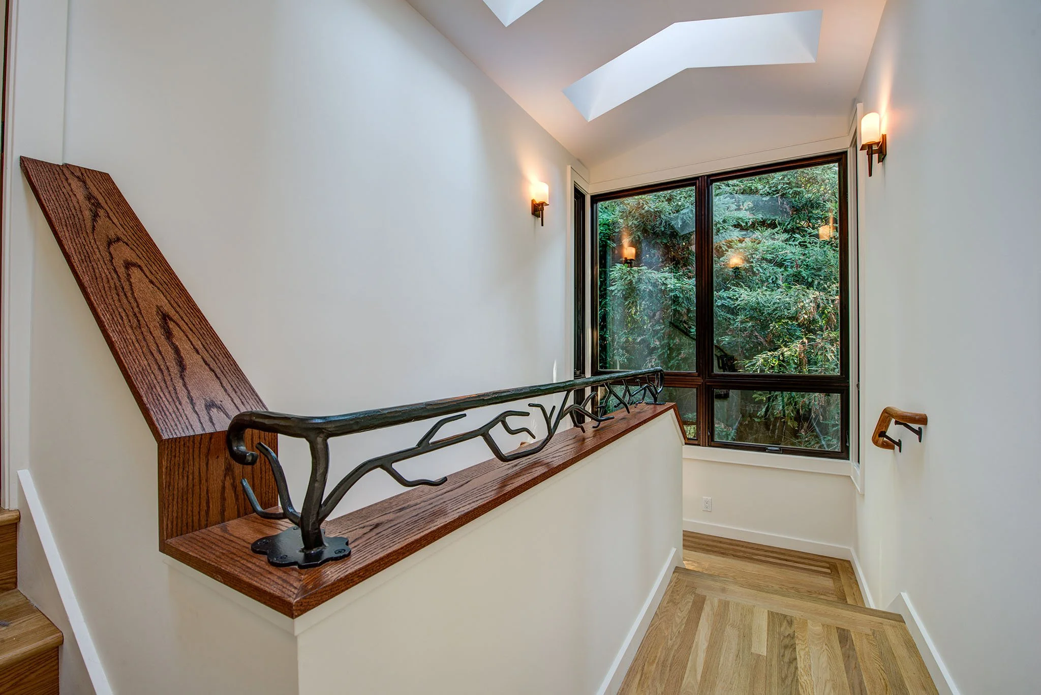 Stair landing with skylights, custom wood handrail, and decorative iron guardrail, bringing natural light into the home and connecting the new second floor addition.