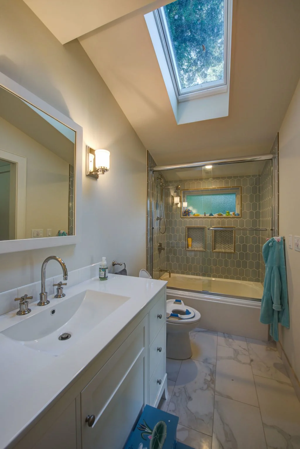 New bathroom with skylight, white vanity, and a tub shower lined in hex tile with built in niches, adding light and function during the Craftsman Renewal remodel.