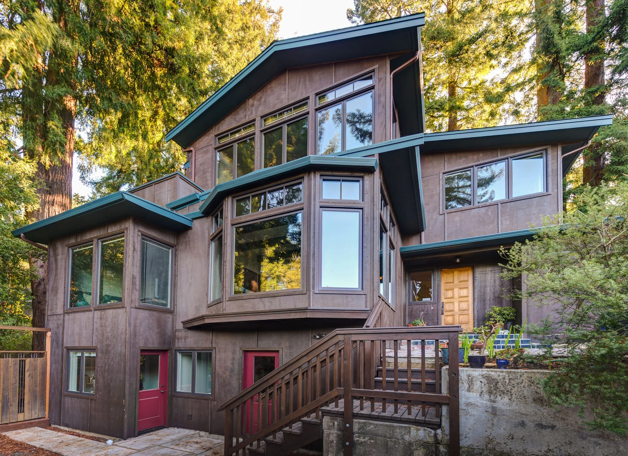 Craftsman home in the Berkeley Hills after Levitch second story addition, showing updated siding, new windows, and entry-deck nestled among tall redwood trees.