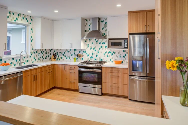 Wide view of the remodeled kitchen opened to the dining room, featuring Levitch built eucalyptus cabinetry, white uppers, stainless appliances, and a green Fireclay Tile backsplash.