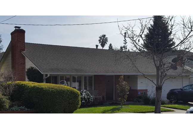 Wide front elevation photo before remodel, showing chimney, single-story profile and landscaping
