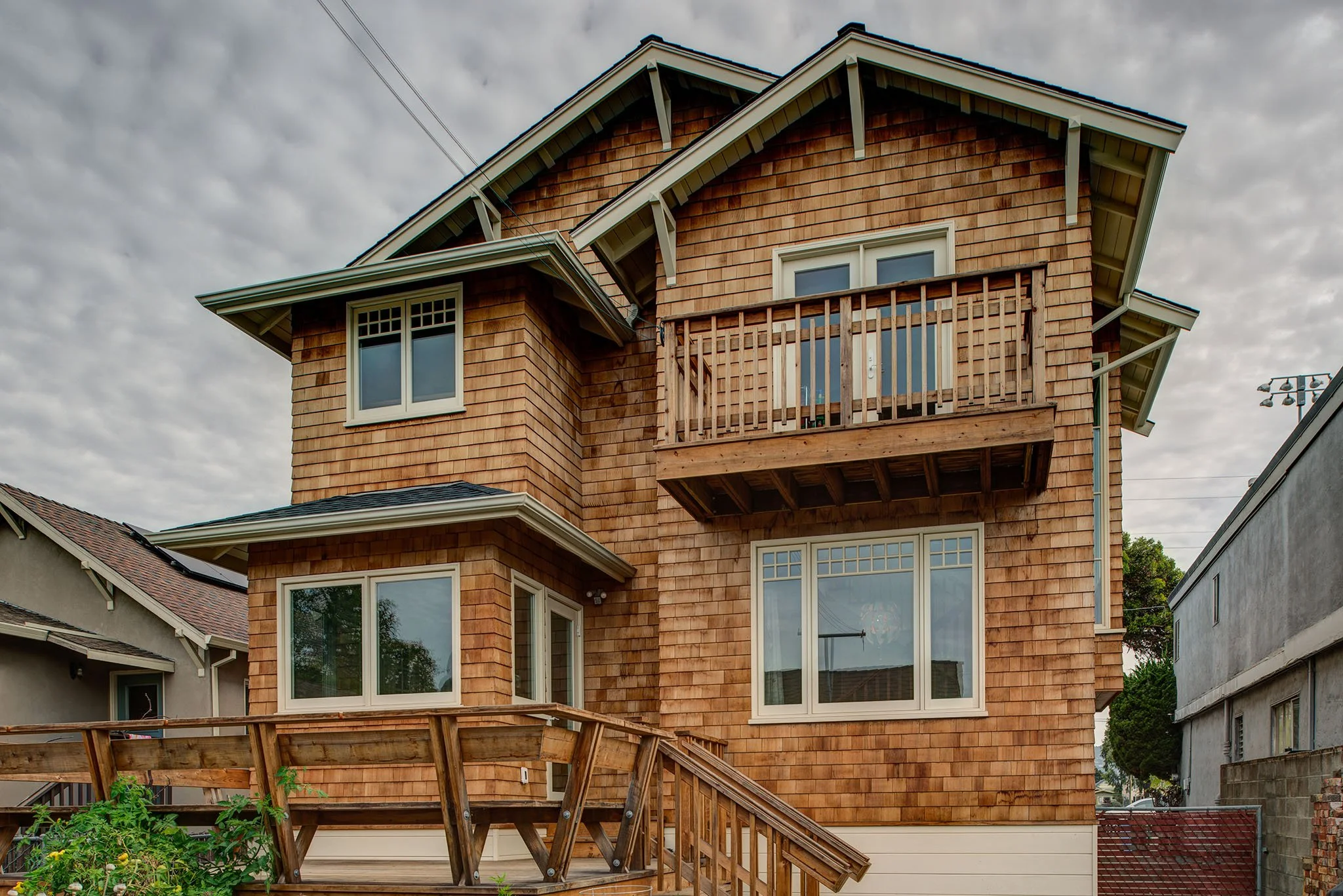Rear exterior showing the two story Craftsman addition with cedar shingle siding, matching roof pitches, large windows, and an upper balcony over the backyard deck.