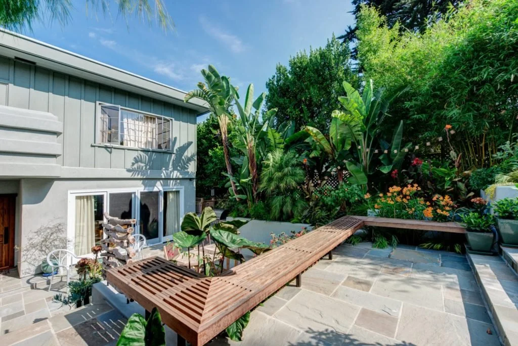 Upper terrace with long built in wood benches, lush planting, and layered garden levels beside the house, showing Levitch terraced outdoor living design for a sloping Bay Area lot.