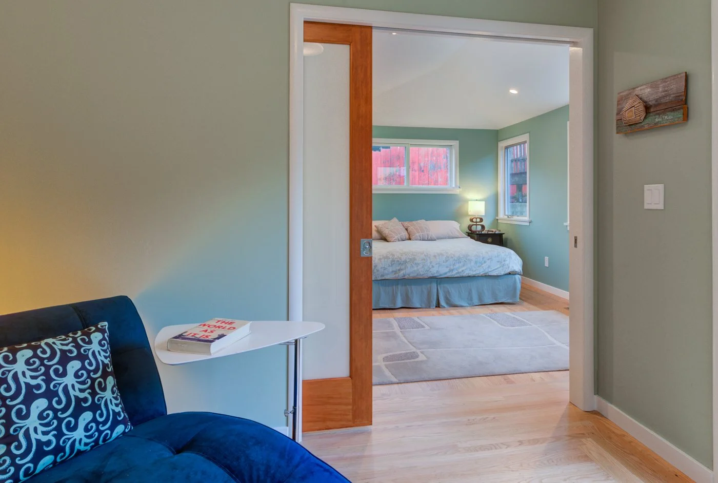 Wood framed sliding door opening to the new bedroom suite, showing fresh flooring and green walls, part of Levitch’s compact addition that adds a primary bedroom and bath.