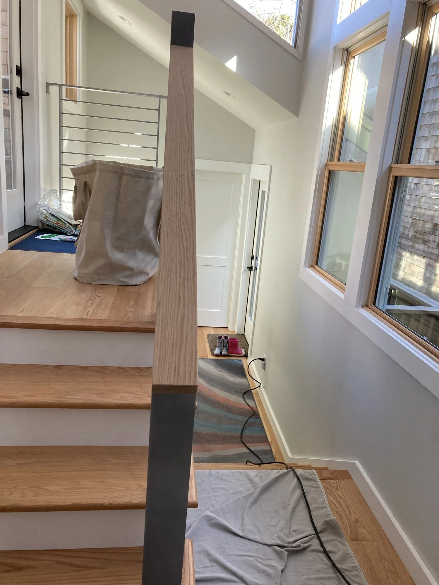 Interior stair hall during construction showing newly installed wood stair treads and metal railing components. Natural light enters through clerestory windows above the split level circulation space.