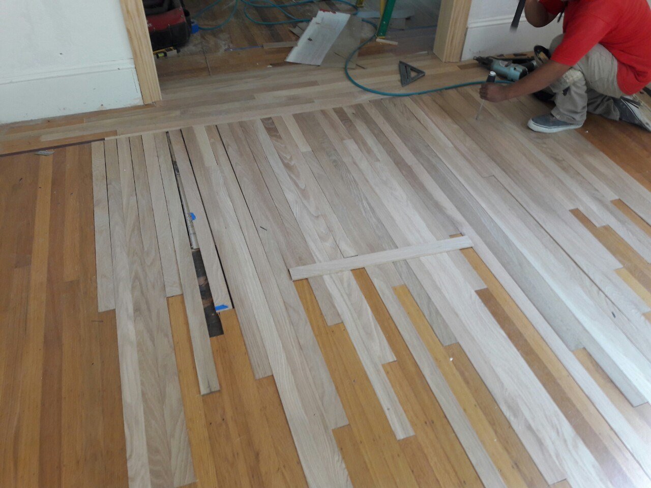 A contractor carefully patches and weaves new hardwood flooring into existing boards during the Lighthearted Kitchen and Family Room Addition renovation.