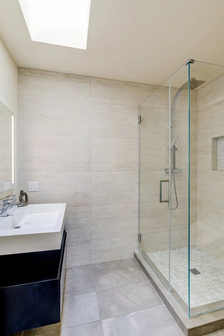 Bathroom with tiled walk-in shower, glass enclosure, skylight above, and modern vanity adjacent to the shower.
