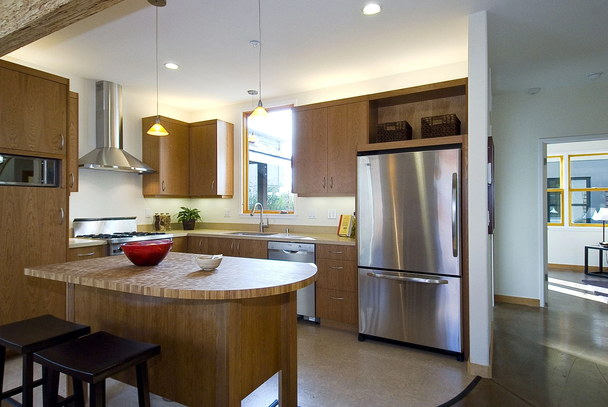 Kitchen view with curved butcher block island, energy efficient appliances, and warm wood cabinetry designed to support everyday cooking while maintaining visual connection to adjacent spaces.