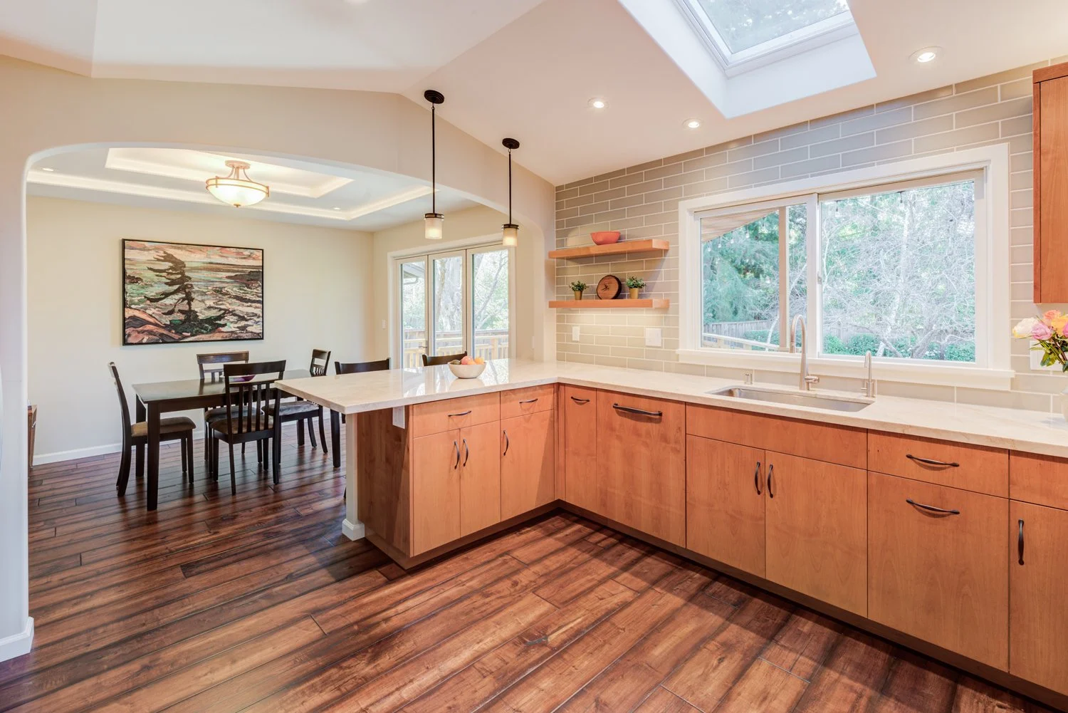 Light-filled kitchen along exterior wall featuring cherry-wood cabinets, integrated lighting, and large window over sink.