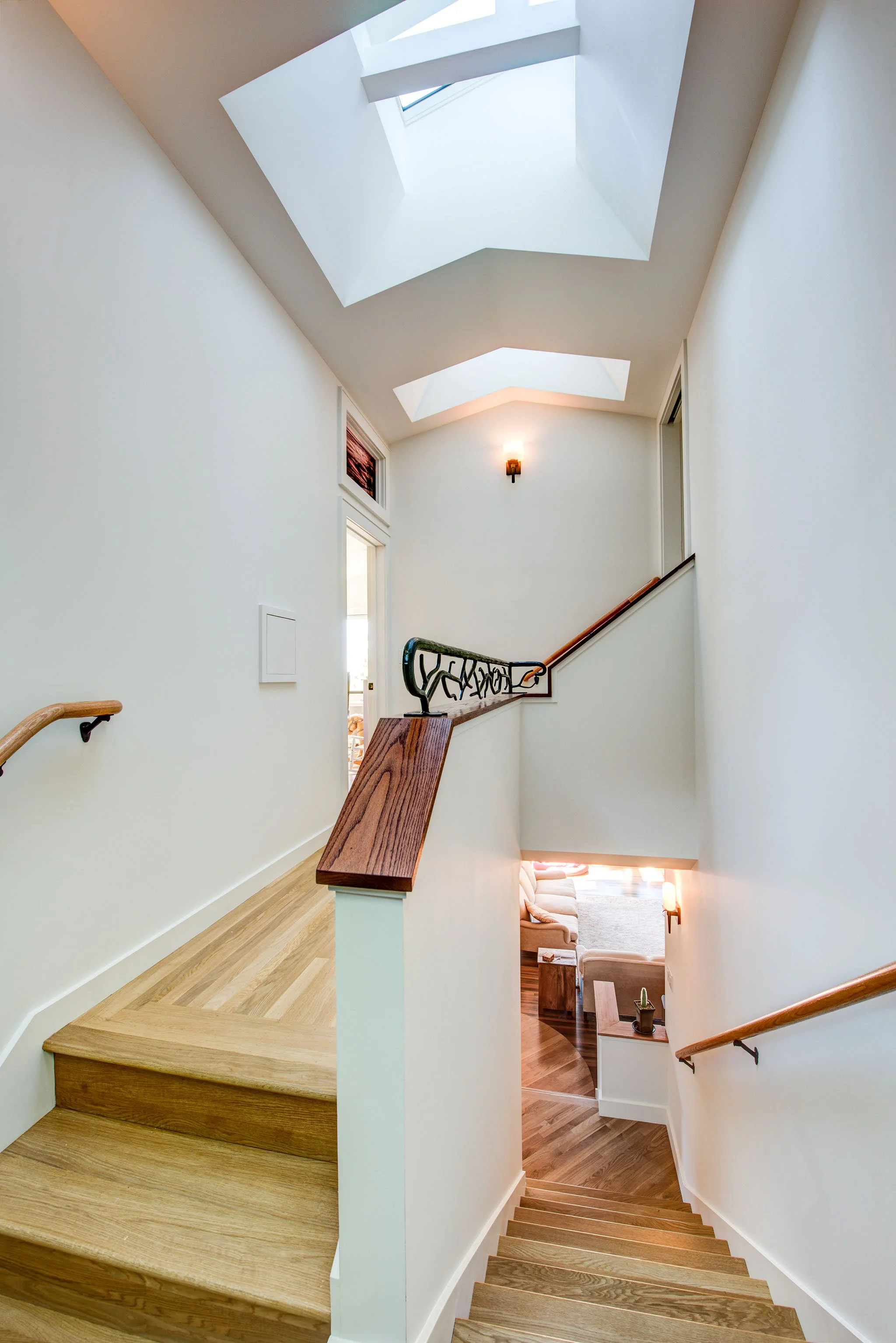 View down the new stairwell with oak treads and skylights overhead, showing bright circulation space created during the Berkeley Hills Craftsman Renewal addition.
