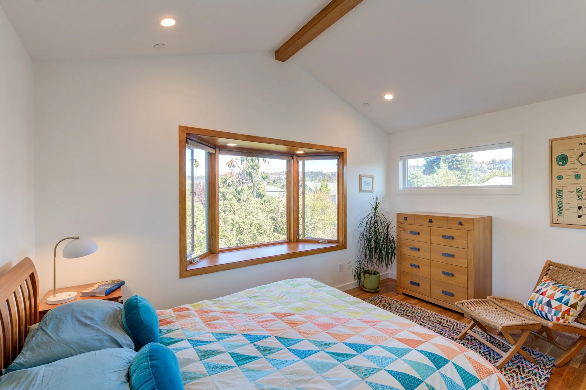 Primary bedroom featuring a vaulted ceiling, custom wood window trim, and views to the surrounding landscape, created as part of the second-story addition.