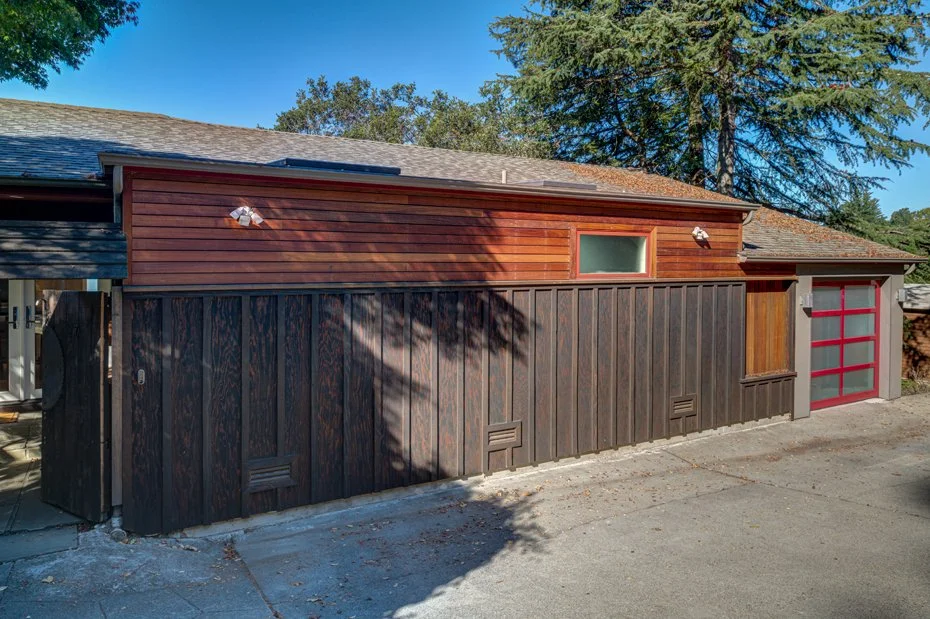 Exterior view showing the converted garage with horizontal wood siding, integrated lighting, and a red-accented garage door.