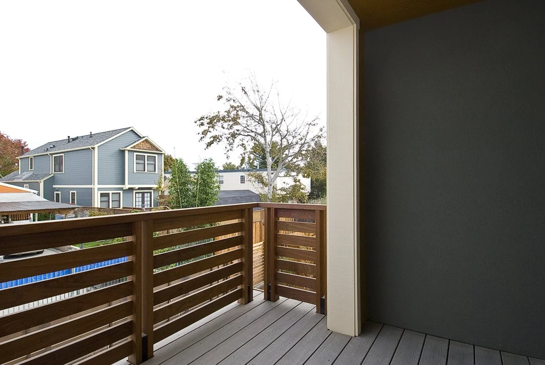 Second story deck with wood railing and durable decking, offering outdoor living space and neighborhood views while supporting the home’s sustainable design goals.