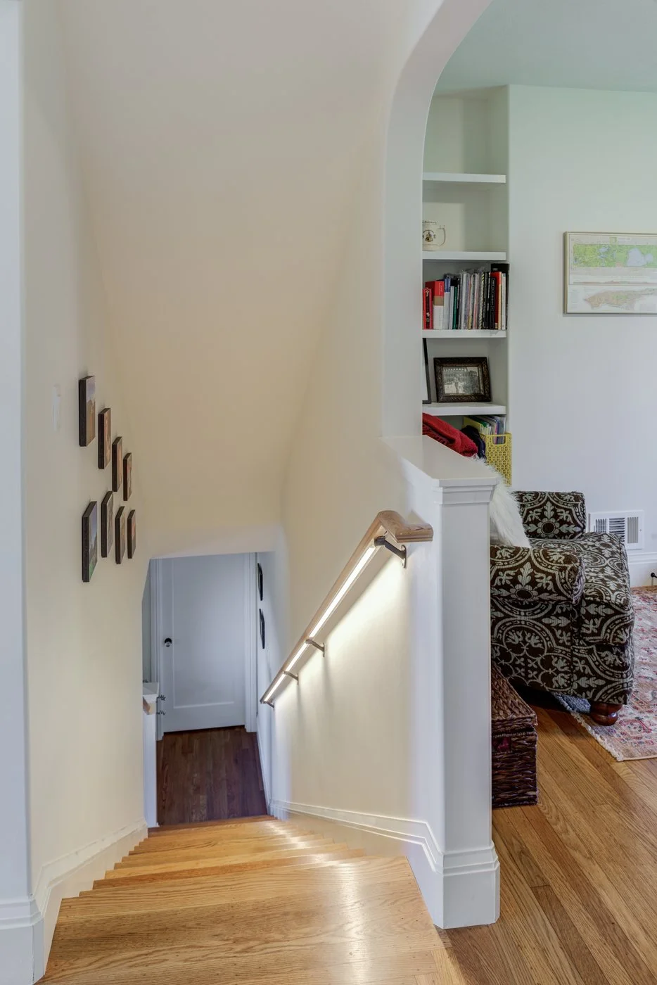 Looking down the main stair after renovations, showing refreshed wood treads, new handrail lighting, and the improved connection between upper bedrooms and the main level.