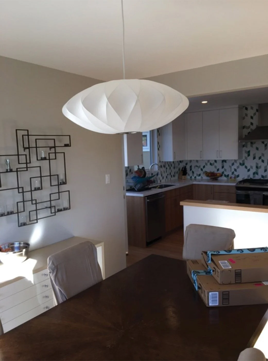 Dining room view into the newly opened kitchen, showing the enlarged opening for better flow, modern pendant light, and the updated eucalyptus cabinets and tile backsplash.