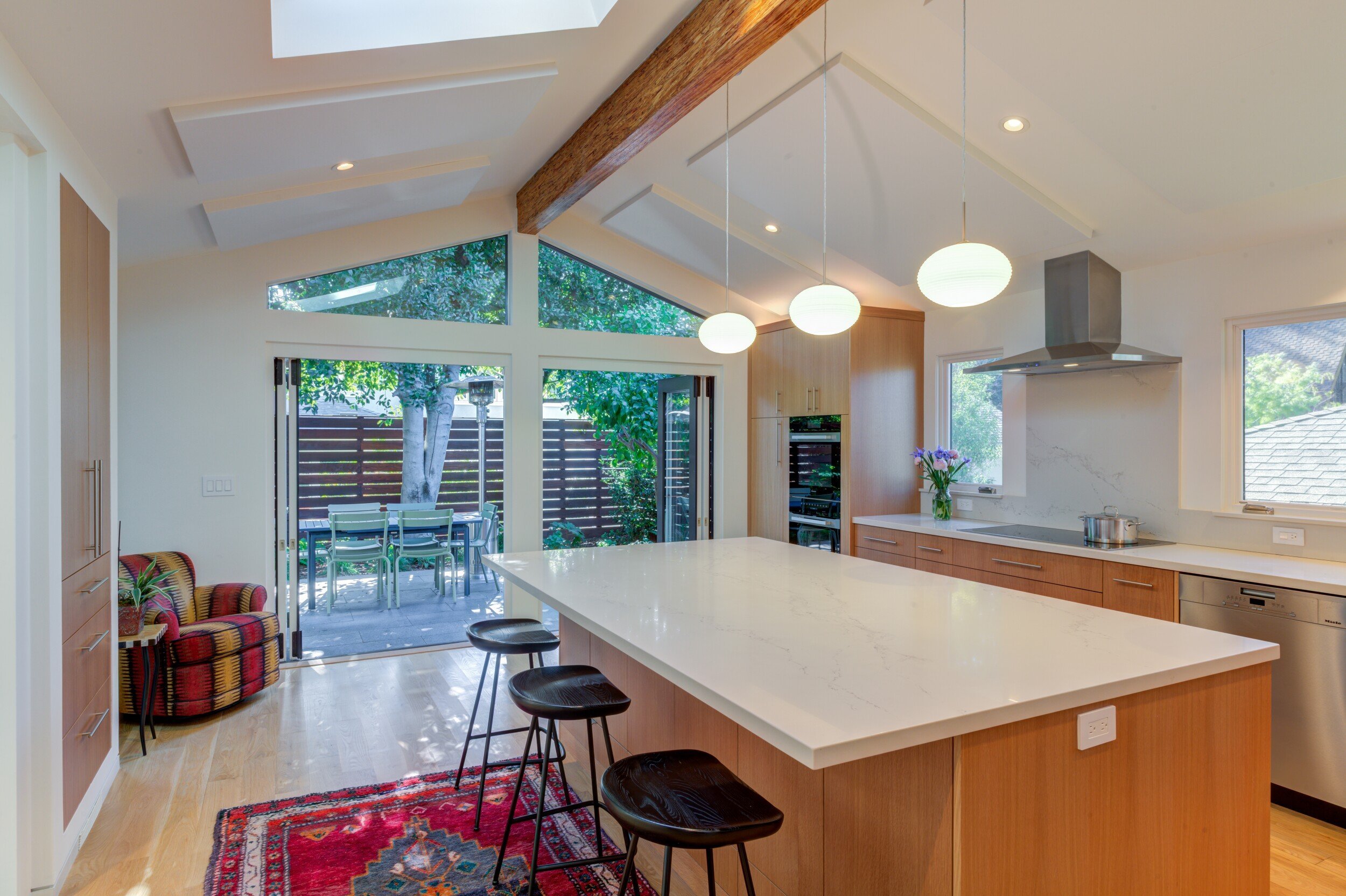 New Kitchen looking past the island with seating toward large windows that face the rear yard, with space for an armchair at the left rear corner