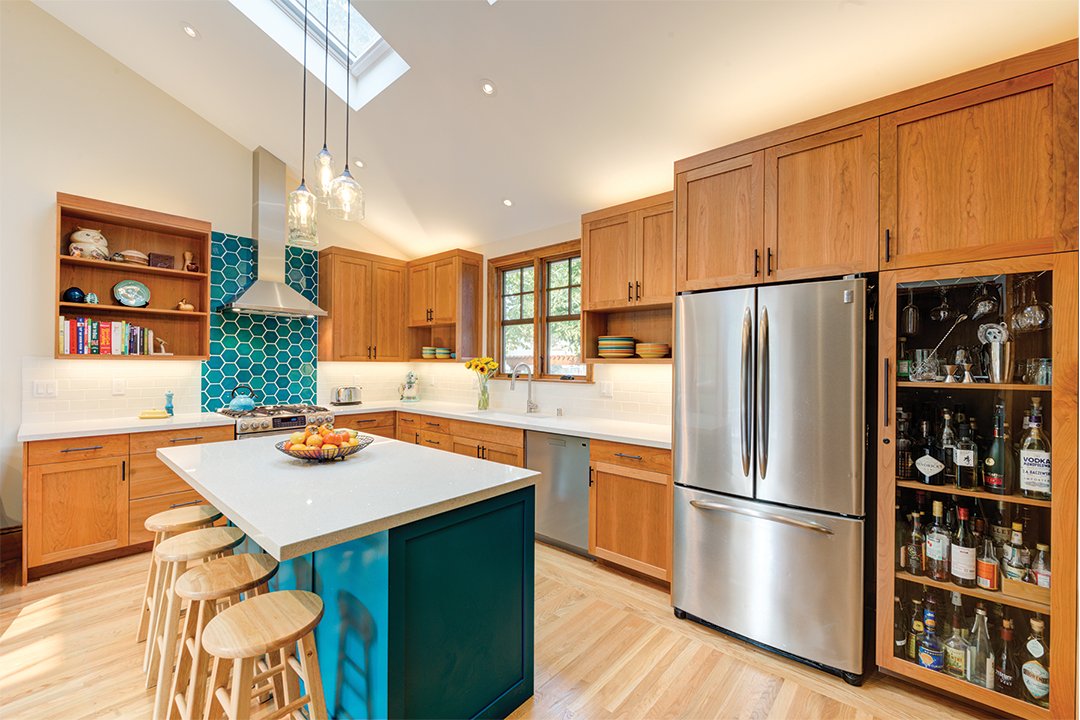 Kitchen and family room connected in an open layout, showing a turquoise island, wood cabinets, vaulted ceiling, and multiple windows and doors that fill the space with daylight.