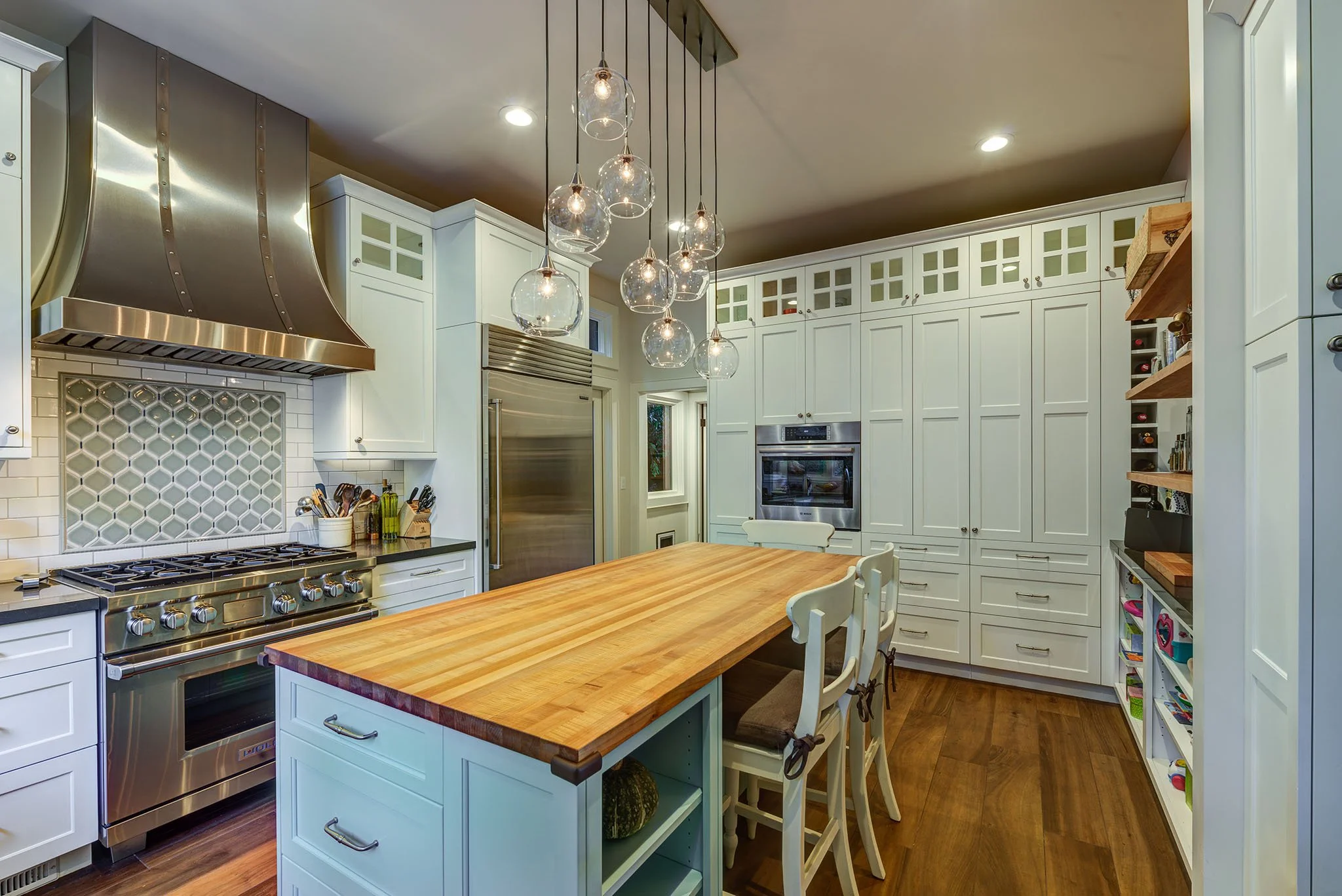 Updated craftsman kitchen with a large butcher block island, stainless range and hood, and tall pantry cabinets, designed by Levitch for better storage and daily cooking.