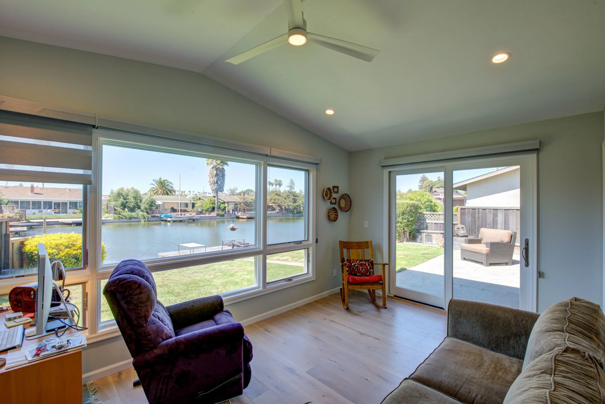 Multipurpose room used as a sitting area and guest space, featuring large windows, light wood floors, and views toward the water and backyard.