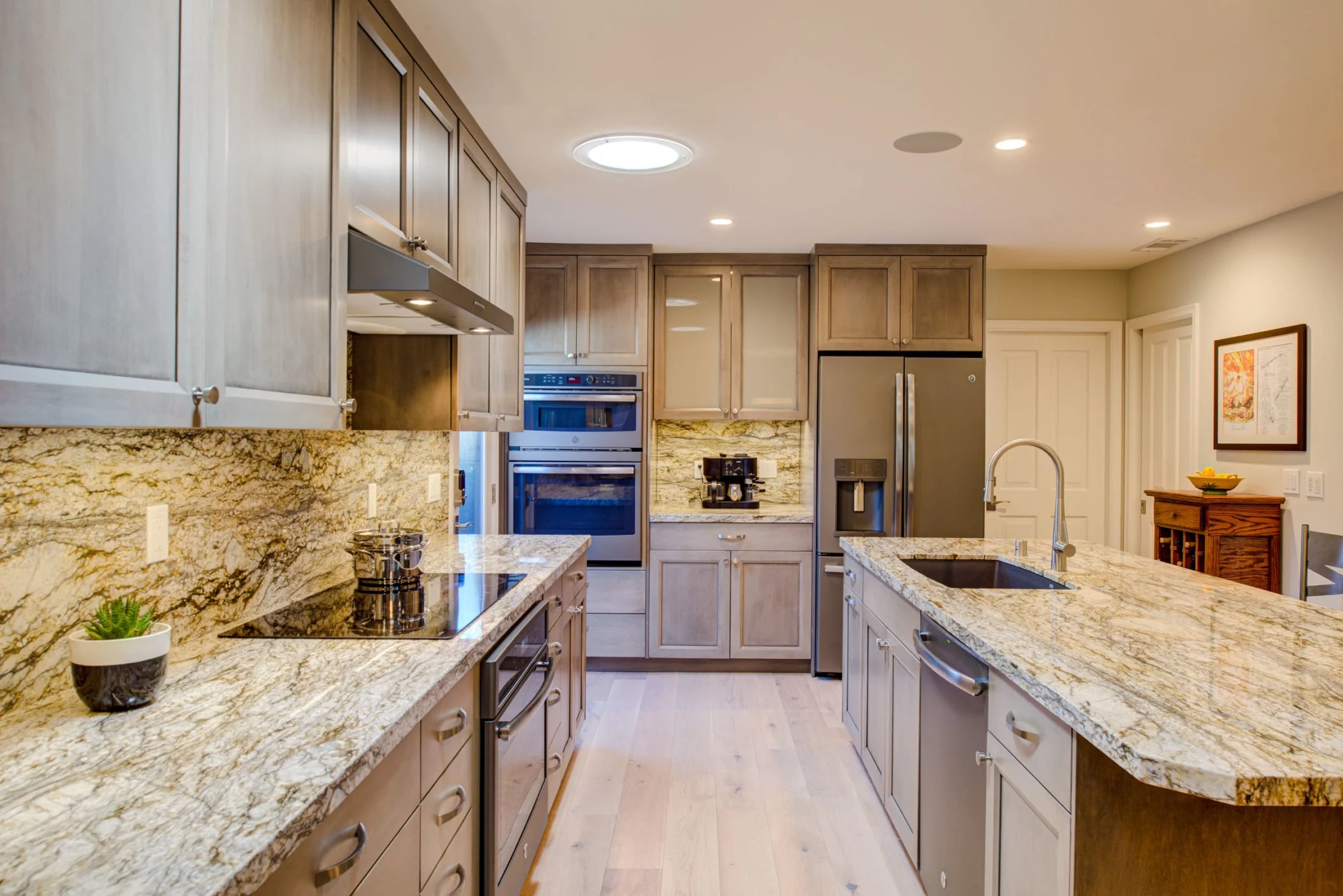 Bright kitchen view showing a large island, stone countertops, skylight, stainless appliances, and improved circulation created by expanding into the former nook.
