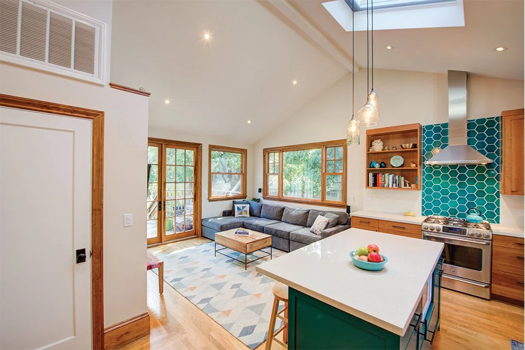 Kitchen opening into the family room, showing a turquoise island, vaulted ceiling with skylight, and glass doors and windows that connect the interior to the yard.