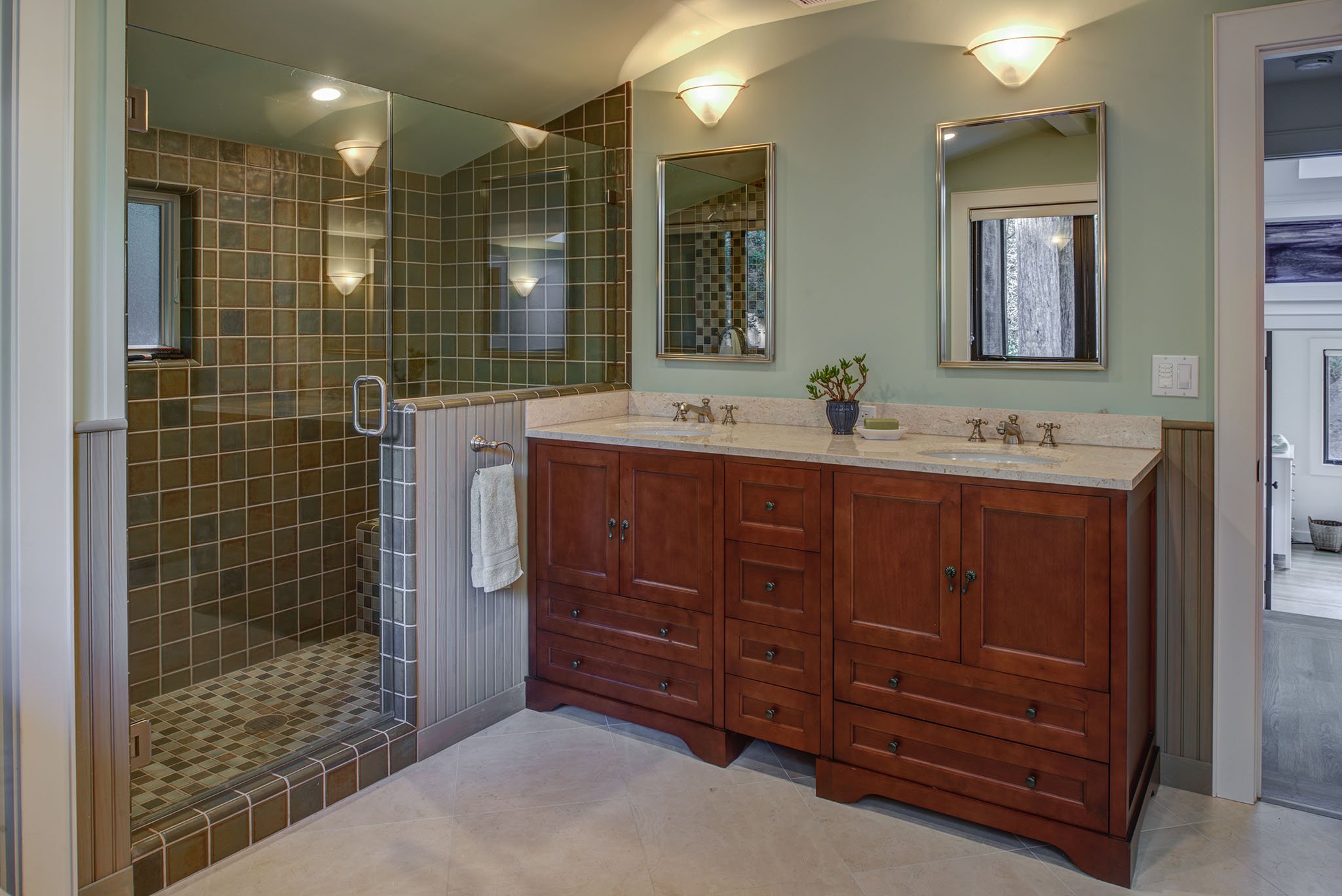 Remodeled primary bathroom with double sinks, wood vanity, and glass shower with tiled walls and mosaic floor, giving the clients added storage and daily comfort.
