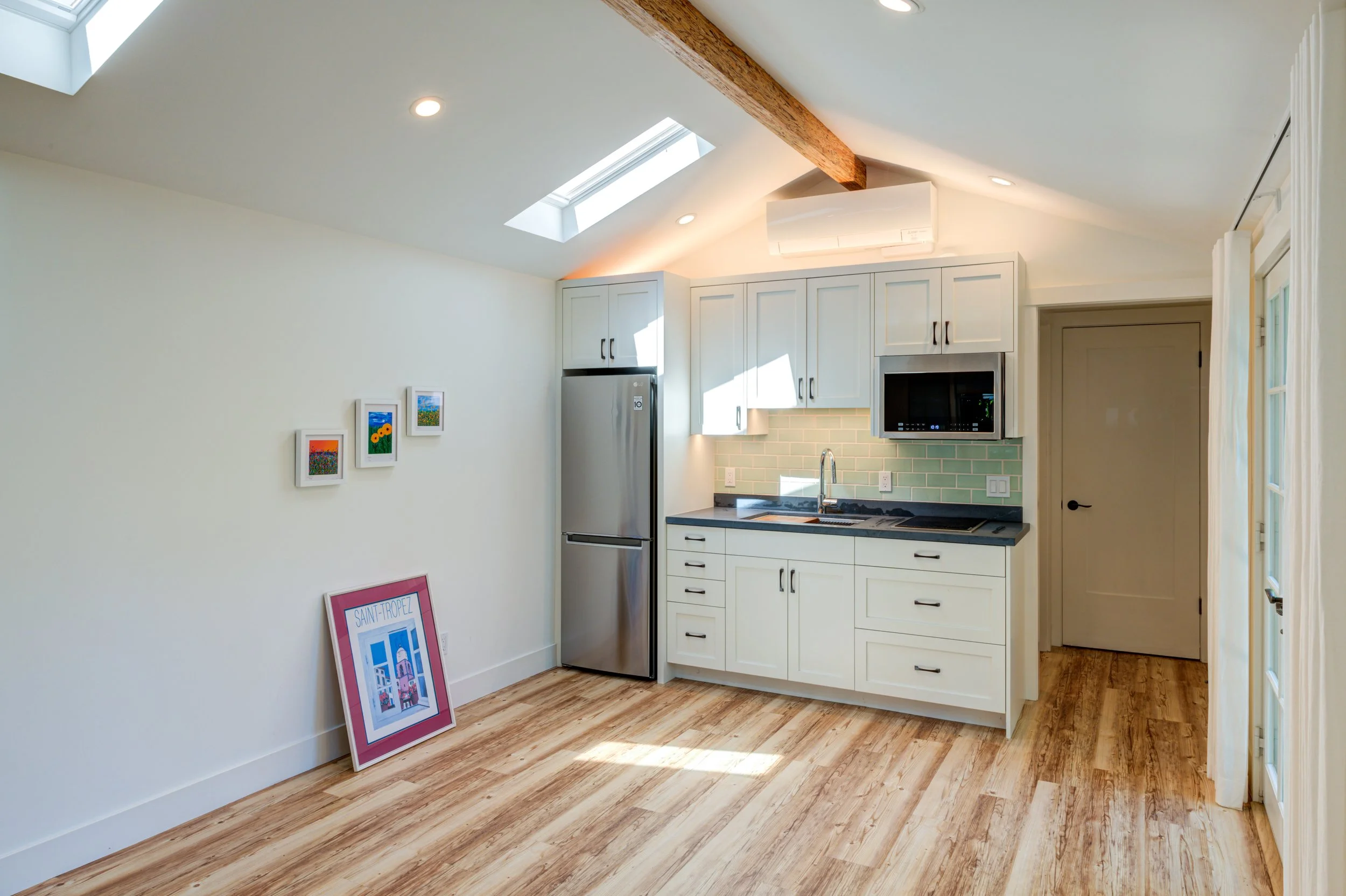 Full new one-wall Kitchen with white cabinetry. Vaulted ceiling with 2 of 3 skylights visible. Hallway to the right of the Kitchen leads to the Bathroom and Closet.