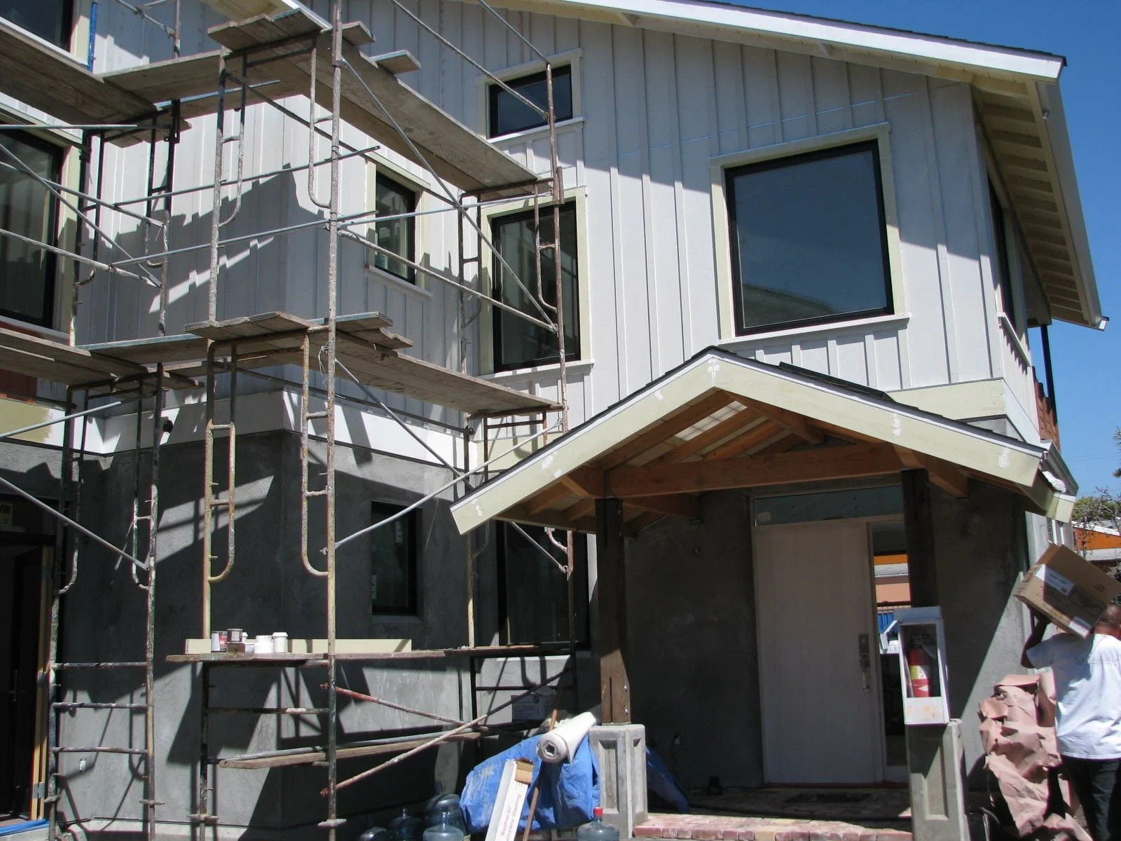 Front entry under construction with scaffolding and newly installed siding, capturing the transition from structural framing to exterior finishes on this energy-efficient residential project.