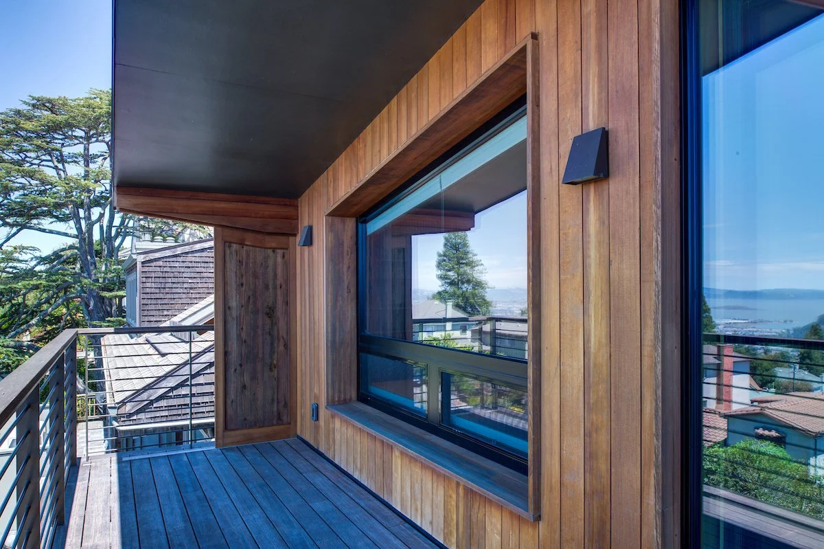Deck with reflected Bay views in the windows. The mix of wood siding, decking, metal sconces and railing is consistent throughout the design.
