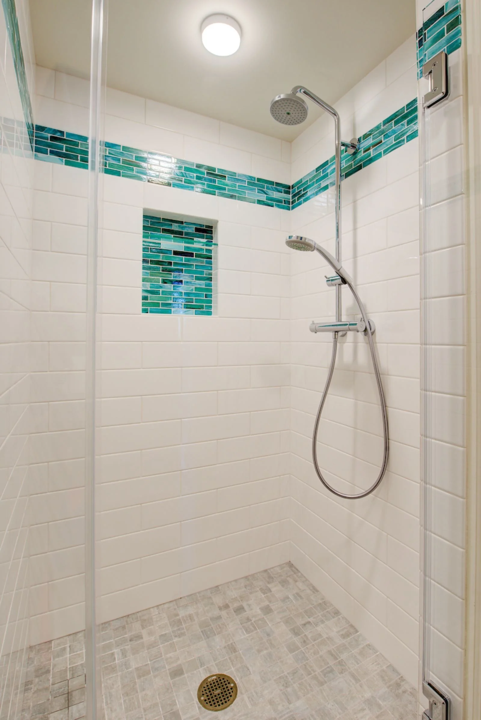 Clean-lined walk-in shower with white subway tile, teal glass accent band and niche, chrome fixtures, and a light mosaic tile floor for a crisp, contemporary spa-like feel.