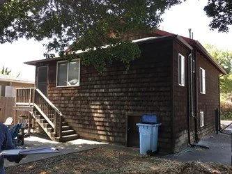 Rear exterior of Berkeley home before renovation, with wood shingle siding, rear stairs, and yard area slated for lift addition and accessibility improvements.