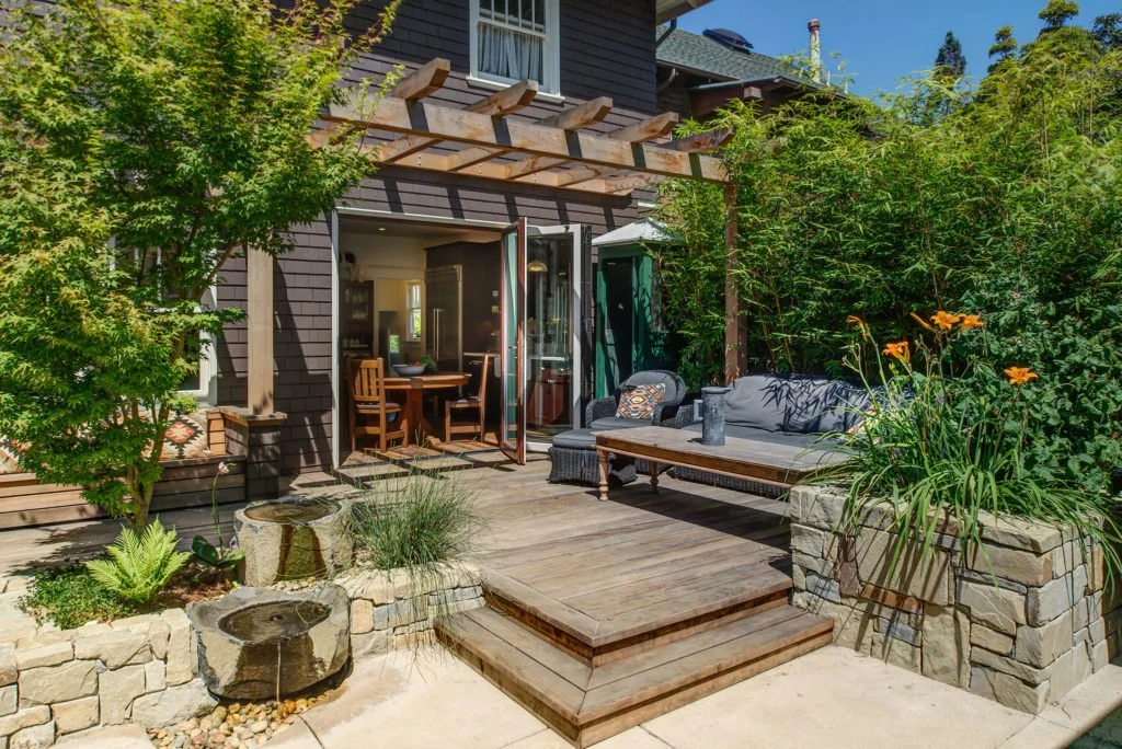 Exterior view of the redwood deck and trellis with the kitchen folding doors being opened, showing the expanded entertaining space designed by the landscape team and built by Levitch.