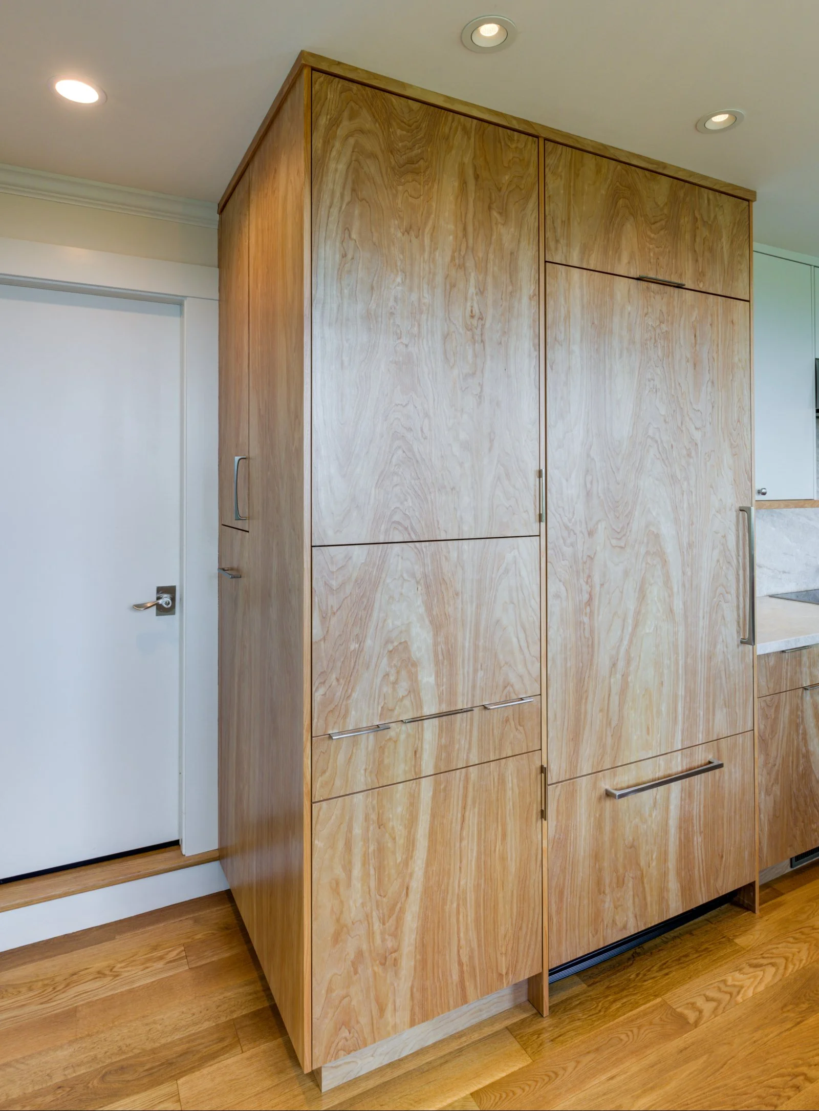 Custom kitchen cabinetry with warm wood veneer panels concealing integrated appliances, creating a clean, modern look that emphasizes craftsmanship, storage efficiency, and seamless design.
