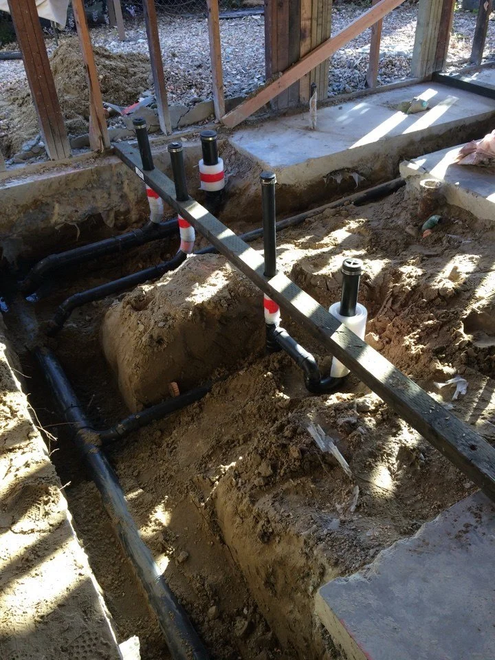 Exposed plumbing trenches during the Alameda waterfront remodel showing new drain and vent lines installed as part of the bathroom and kitchen reconfiguration.