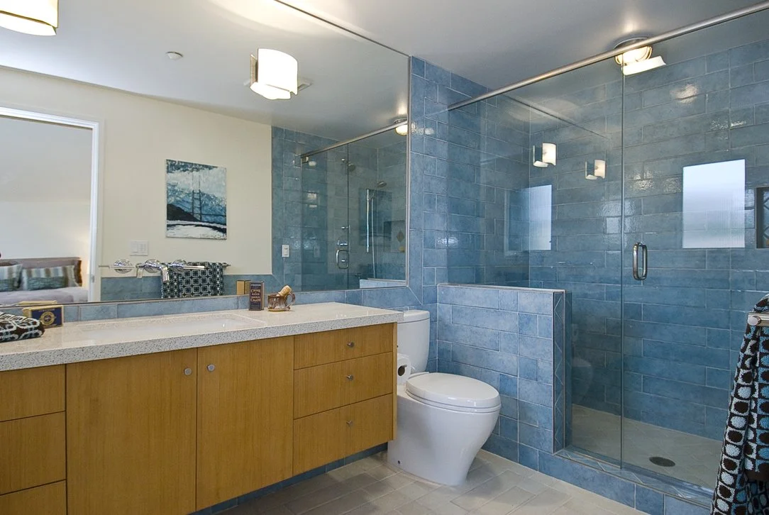 Bathroom with blue tile shower walls, glass enclosure, and custom wood vanity, combining durable materials with a clean modern layout designed for long-term residential use.