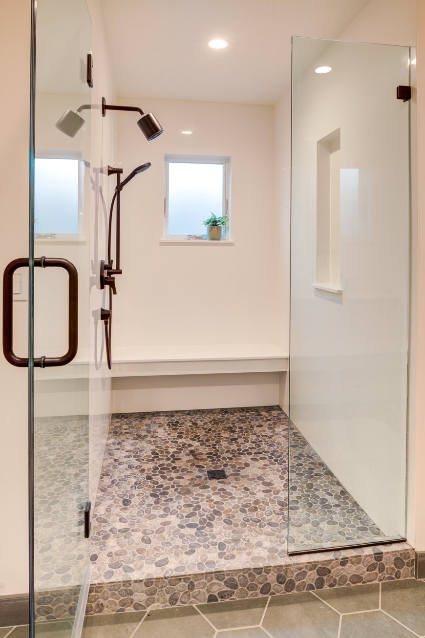 Walk-in shower with glass enclosure, built-in bench, and pebble tile floor, designed for comfort and accessibility for family members of all ages in the new bathroom addition.