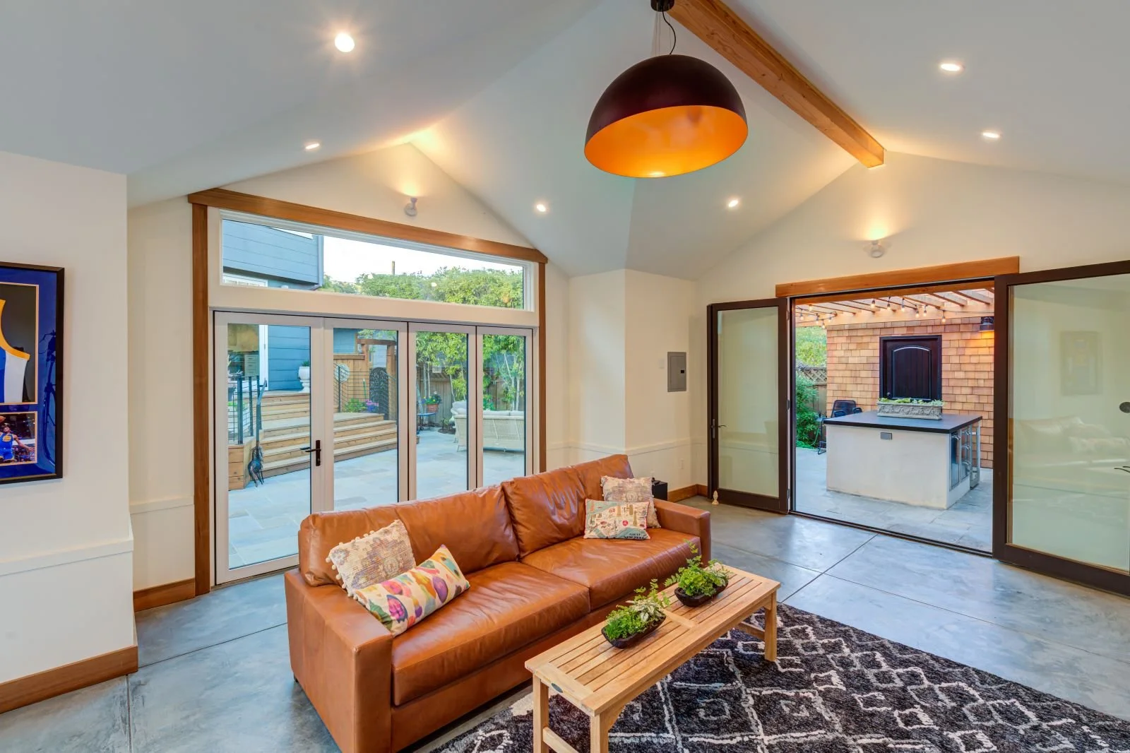 The interior living space features a vaulted ceiling with exposed wood beams, concrete flooring, and large glazed openings that frame views back to the courtyard, supporting indoor–outdoor flow and everyday living.