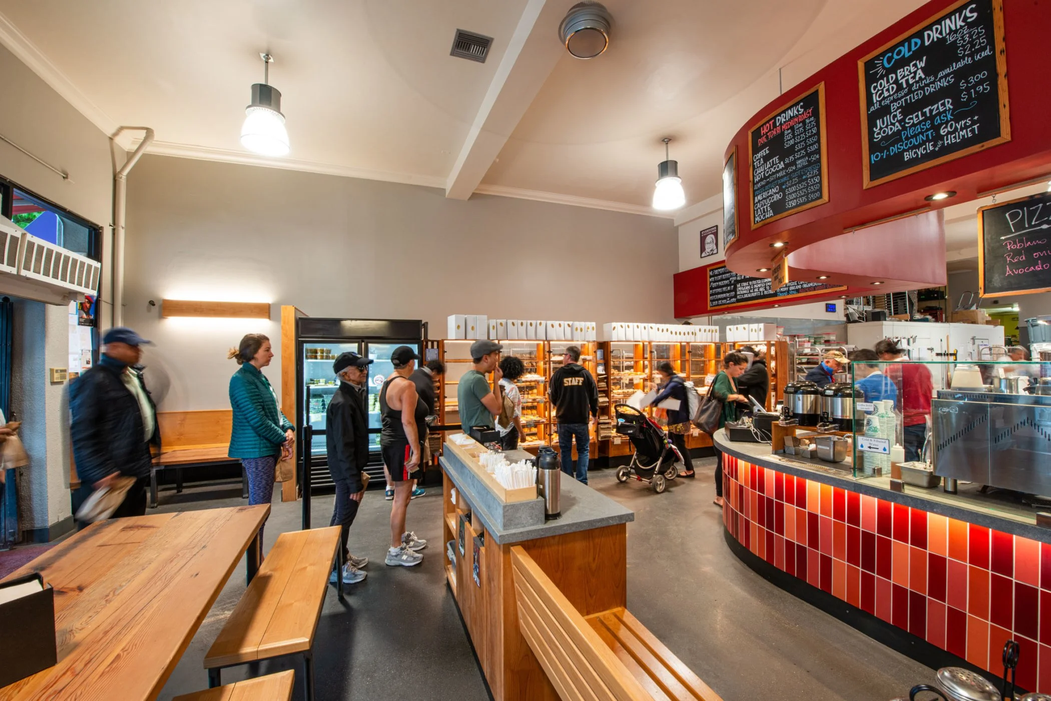 Arizmendi Bakery Customer Area looking from front side across seating, point of sale area, customers and bakery items in custom self-serve cases.