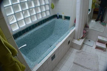 Original bathroom before renovation, featuring a built-in blue bathtub, dated tile, and limited natural light prior to the remodel.
