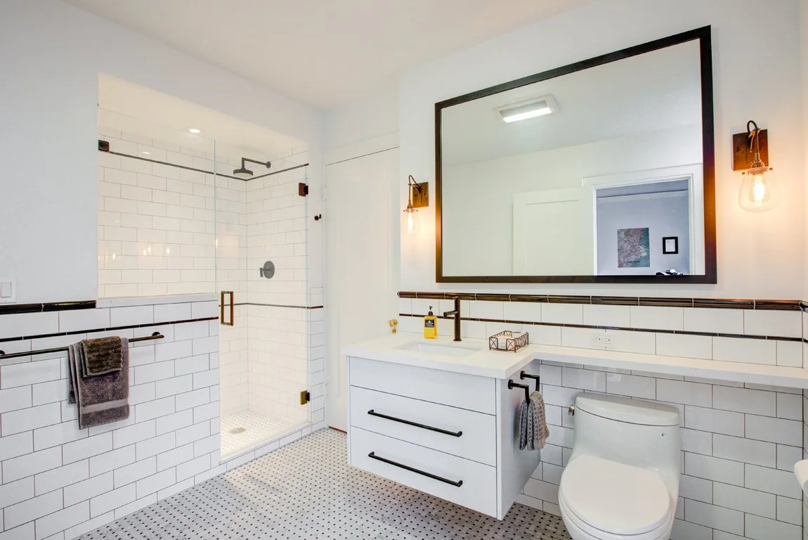 Remodeled guest ‘Jack and Jill’ bathroom with white tile walls, black accents, glass shower enclosure, and a floating vanity.
