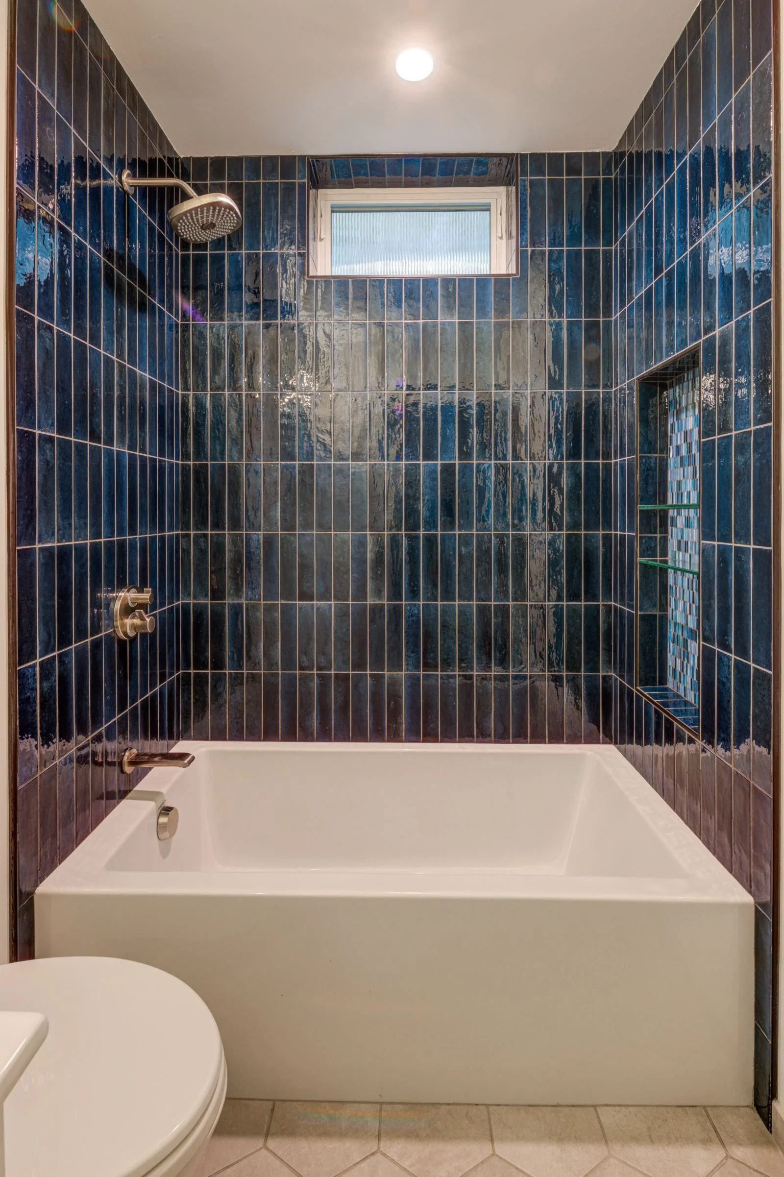 Lower Bathroom showcasing variegated dark blue tiles surrounding the tub/shower. The high window above brings in natural light while maintaining privacy.