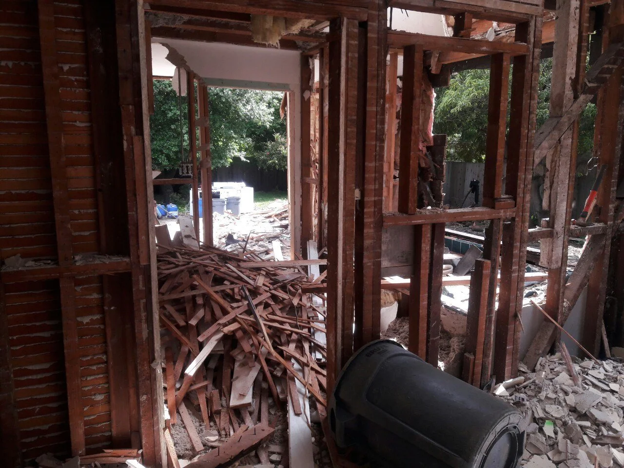 Interior demolition in progress, with wall framing exposed and debris on the floor as part of opening the home for the new addition and layout changes.