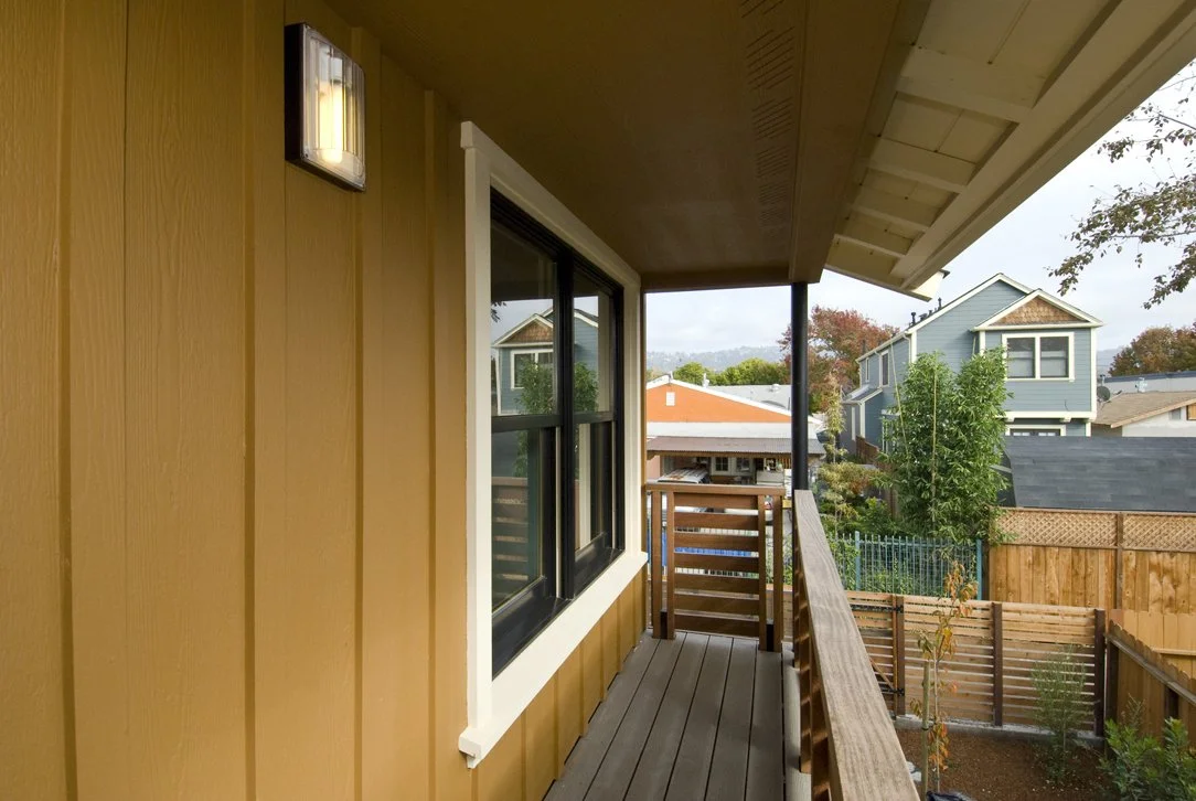 Upper level covered porch with wood railing and neighborhood views, providing a shaded outdoor extension of the home that enhances natural ventilation and connection to the outdoors.